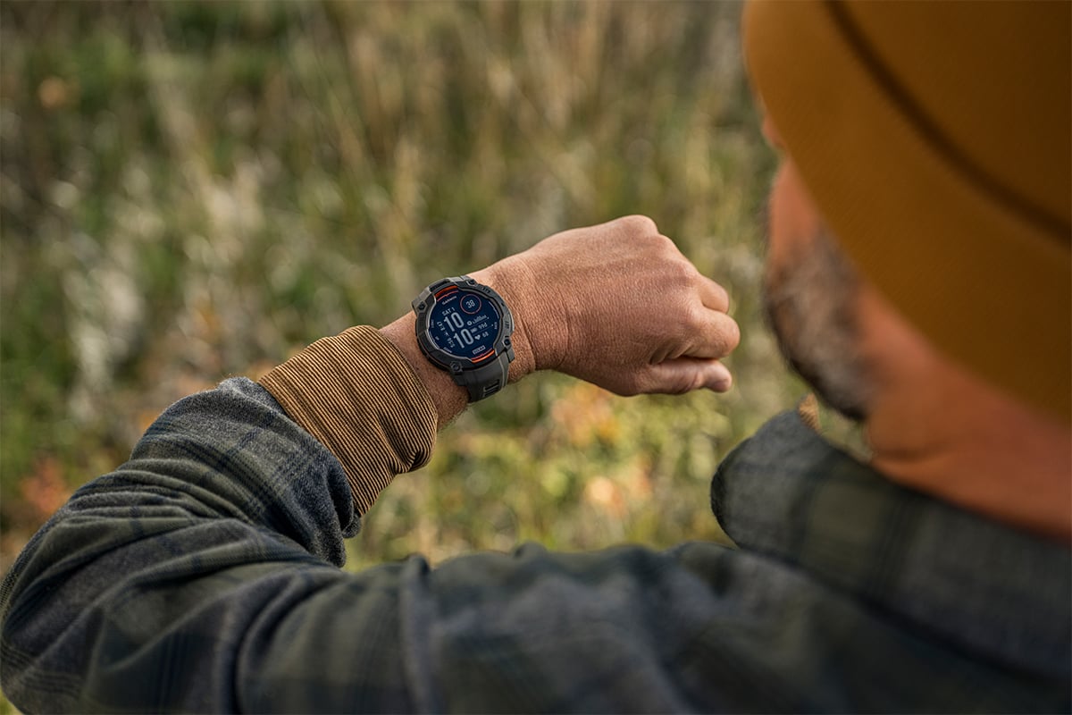 A man wearing a flannel shirt checks the time on his Garmin Instinct 3 smartwatch.