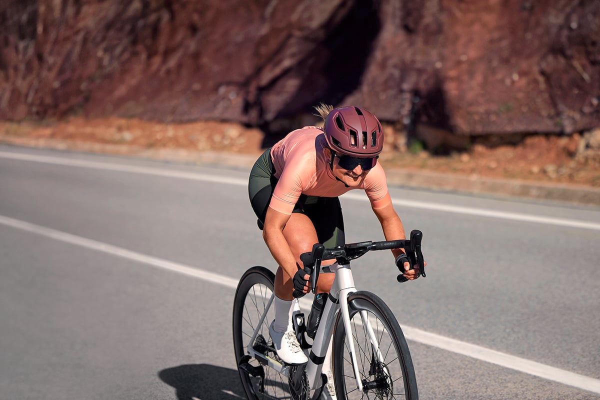 A woman wearing a maroon helmet cycles down a road.