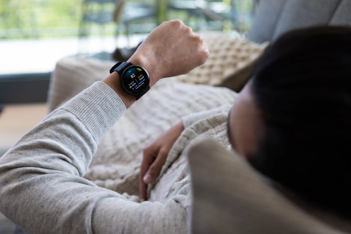 A man in a gray shirt on a couch looks at his Garmin sleep score of 82.