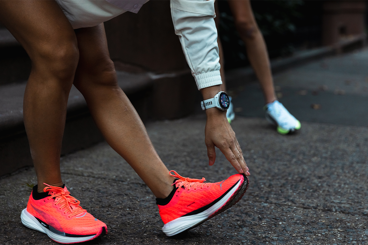 A woman wearing a Garmin smartwatch on her wrist touches the toe of her shoe to stretch.