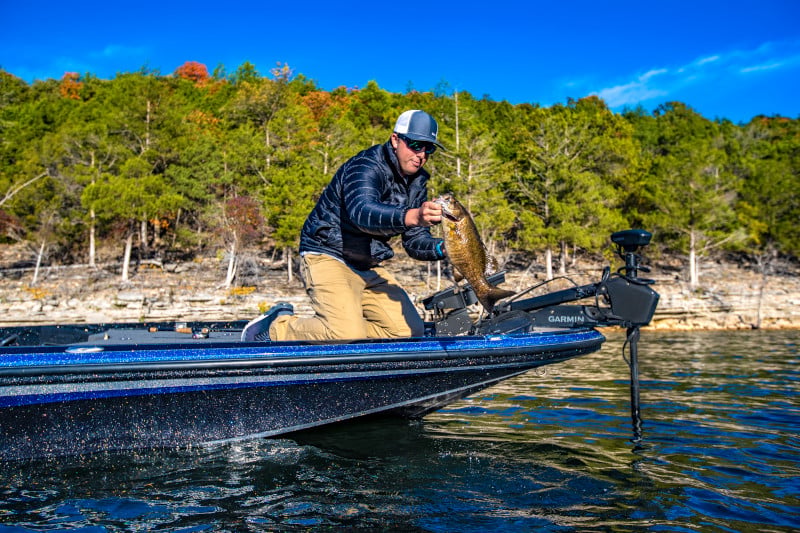 Man out on the water at the edge of his boat holding a fish.