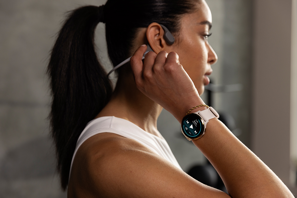 A woman wearing a Garmin Venu 3 smartwatch places a headphone in her ear.