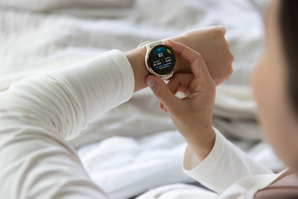 A woman in a white shirt checks her sleep score of 82 on her Garmin Venu 3.