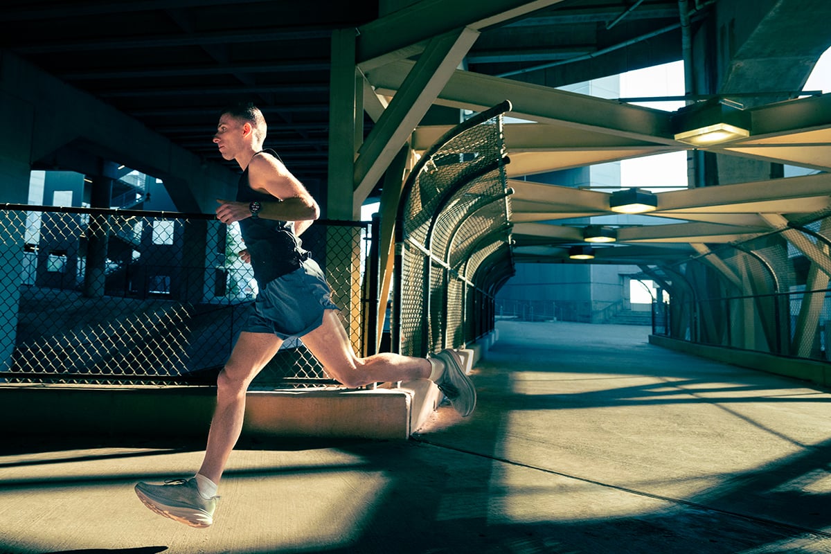 A man wearing blue shorts and a black tank top, along with a Garmin Forerunner 970 smartwatch, runs along a path.